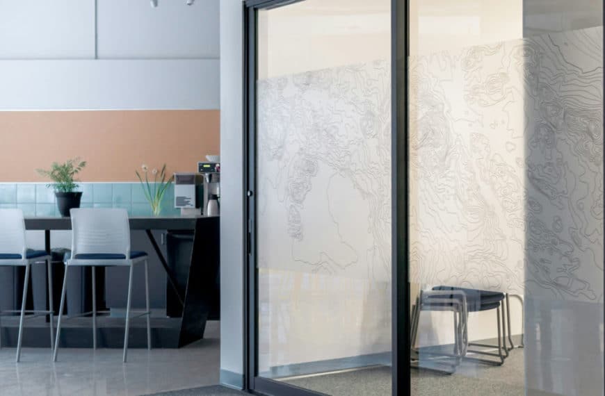 Un Espace De Bureau Moderne Avec Une Porte Vitrée, Des Chaises Blanches, Une Petite Table Et Des œuvres D'art Murales Représentant Des Lignes Abstraites Ressemblant à Des Cartes.