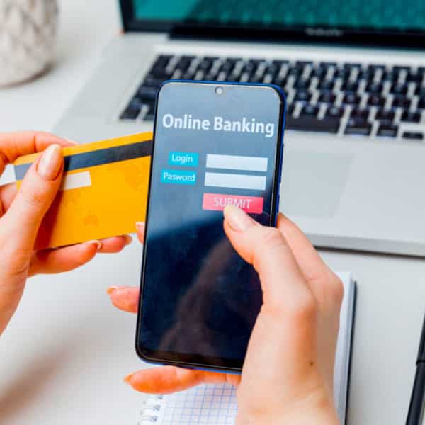 Une Personne Tenant Une Carte De Crédit Et Un Smartphone Affichant Un écran De Connexion Bancaire En Ligne, Avec Un Ordinateur Portable En Arrière Plan.
