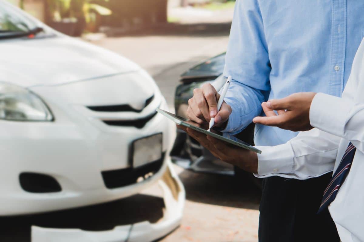 Deux Personnes Se Tiennent à Côté De Voitures, L'une Tenant Un Presse Papiers Tandis Que L'autre Signe Un Document, Peut être Pour Une Assurance Automobile Ou Un Rapport D'accident.