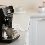 Une Tasse De Café Est Posée Sur Le Plateau D'une Machine à Café Automatique Noire Sur Un Comptoir De Cuisine, Avec Des Pots Et Des Plats En Arrière Plan.