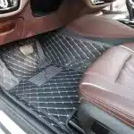 L'image Montre La Zone Passager Avant D'un Intérieur De Voiture Avec Des Tapis De Sol Matelassés Foncés Et Des Sièges En Cuir Marron.
