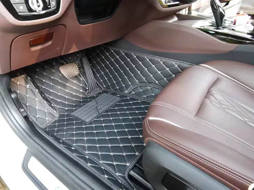 L'image Montre La Zone Passager Avant D'un Intérieur De Voiture Avec Des Tapis De Sol Matelassés Foncés Et Des Sièges En Cuir Marron.