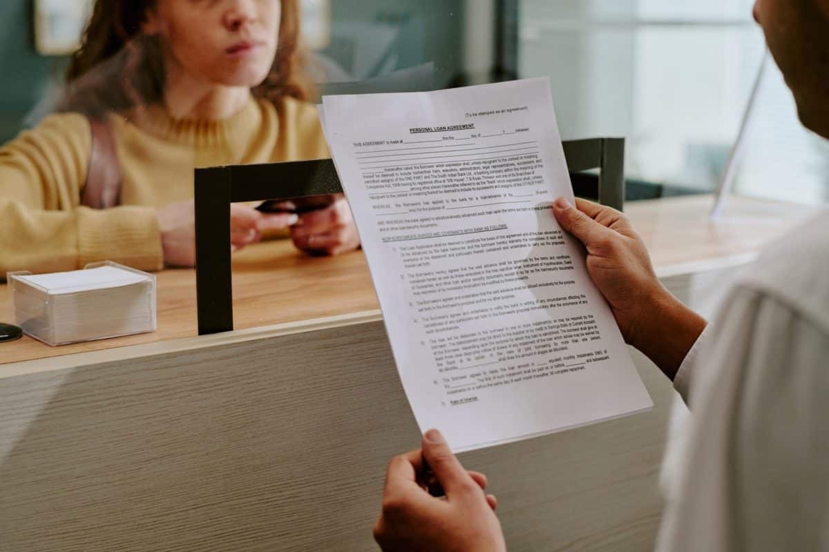 Une Personne Remet Un Document à Une Femme Debout à Un Comptoir De Service, Qui Tient Sa Carte D'identité.