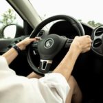 Personne Portant Une Chemise Blanche Tenant Le Volant D'une Voiture Volkswagen, Photographiée Depuis Le Siège Passager.