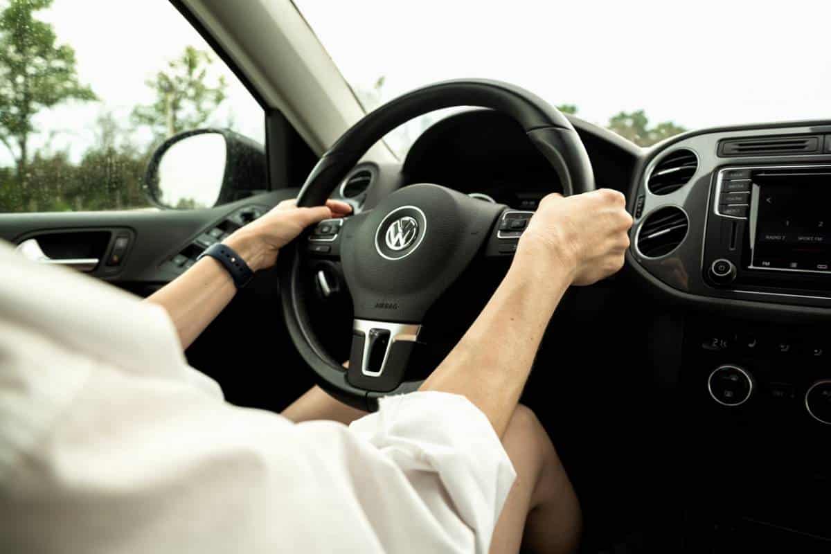 Personne Portant Une Chemise Blanche Tenant Le Volant D'une Voiture Volkswagen, Photographiée Depuis Le Siège Passager.