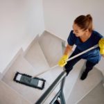 Une Femme Portant Des Gants Et Une Chemise Bleue Nettoie Un Escalier Avec Une Serpillière Plate.
