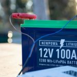 Gros Plan D'une Batterie Au Lithium Newpowa 12v 100ah Avec Ses Câbles Rouge Et Noir, Placée à L'extérieur Sur Une Surface.