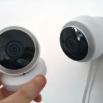Une Main Tient Une Caméra De Sécurité Ronde à Côté D'une Caméra Similaire Montée Sur Un Mur Blanc.