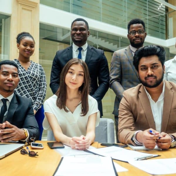 Sept Personnes Habillées Professionnellement Posent Pour Une Photo De Groupe à Une Table De Conférence Avec Des Ordinateurs Portables, Des Documents Et Des Stylos Dans Un Bureau Moderne.