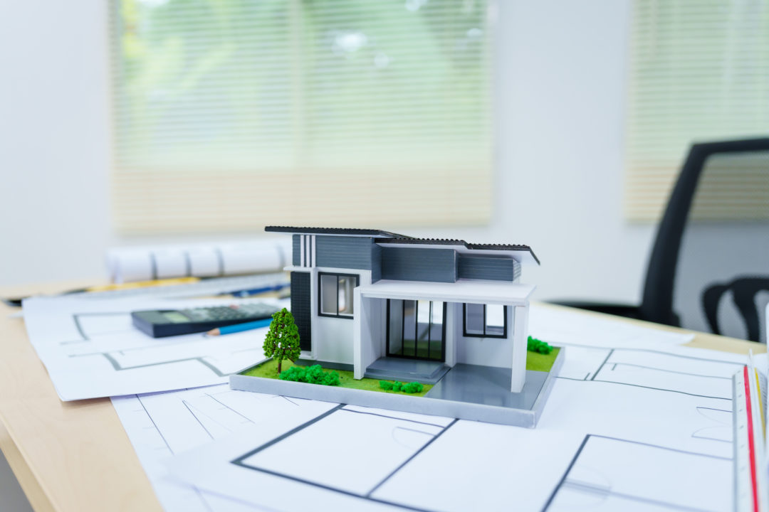 La Maquette D'une Maison Moderne Est Posée Sur Des Plans D'architecte Sur Un Bureau, Avec Une Calculatrice Et Une Chaise De Bureau à L'arrière Plan.