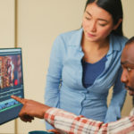 Un Homme Montre Une Ligne De Temps De Montage Vidéo Sur Un écran D'ordinateur Tandis Qu'une Femme Se Tient à Côté De Lui, Tous Deux Concentrés Sur L'écran.