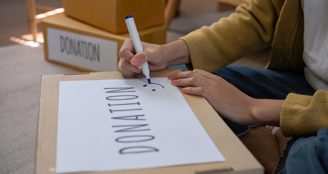 Une Personne écrit Au Marqueur Sur Une Boîte En Carton Portant L'inscription "don". D'autres Boîtes Portant Des étiquettes Similaires Se Trouvent à L'arrière Plan.