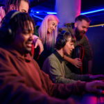 Focused Interracial Gamers Playing Online Battle While Friends W