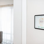 Un Thermostat Numérique Monté Sur Un Mur Blanc Affiche Une Température Ambiante De 22,0°c Dans Un Salon Moderne Et Lumineux.