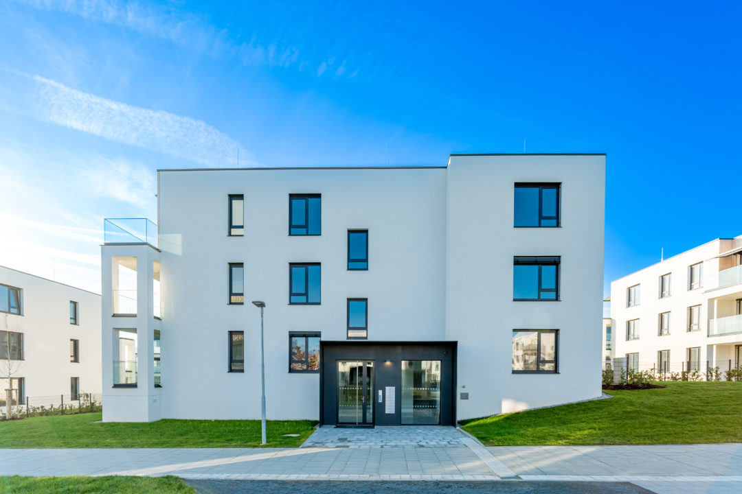 Immeuble Moderne De Trois étages Avec Un Extérieur Blanc, De Grandes Fenêtres Et Une Pelouse Sous Un Ciel Bleu Clair.
