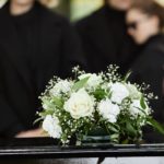 Fleurs Blanches Sur Un Cercueil Avec Deux Personnes En Vêtements Noirs S'embrassant à L'arrière Plan Lors D'un Enterrement.