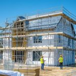 Une Maison En Construction Entourée D'échafaudages ; Deux Ouvriers Du Bâtiment Portant Des Gilets De Sécurité Et Des Casques Travaillent Sur Le Chantier.
