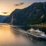Navire de croisière blanc naviguant dans un fjord norvégien au coucher du soleil. Montagnes verdoyantes, cascades et village côtier.
